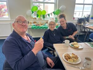 Group of three, two service users and a staff member smiling at the camera with green decorations in the background.